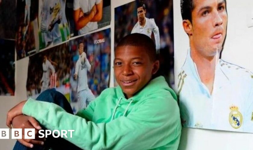 Kylian Mbappe sits on his bed with posters of Real Madrid's Cristiano Ronaldo all around him