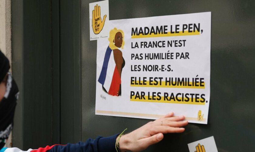 Un manifestant colle une affiche clamant "Madame Le Pen, la France n'est pas humiliée par les noirs, elle est humiliée par les racistes" sur le siège du Rassemblement national lors d'une manifestation de SOS Racisme en soutien à la chanteuse Aya Nakamura, à Paris, le 24 mars 2024