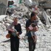 Un couple palestinien tenant ses enfants dans les bras marche au milieu des destructions à Khan Younès, dans le sud de la bande de Gaza, le 4 juillet 2024