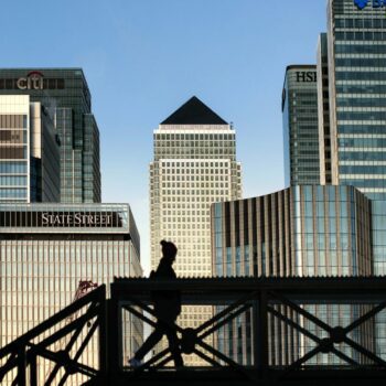 An early morning walker on a bridge in front of the Canary Wharf skyline, in East London.