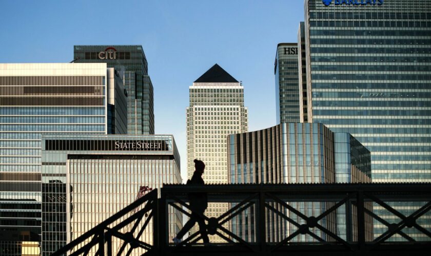 An early morning walker on a bridge in front of the Canary Wharf skyline, in East London.