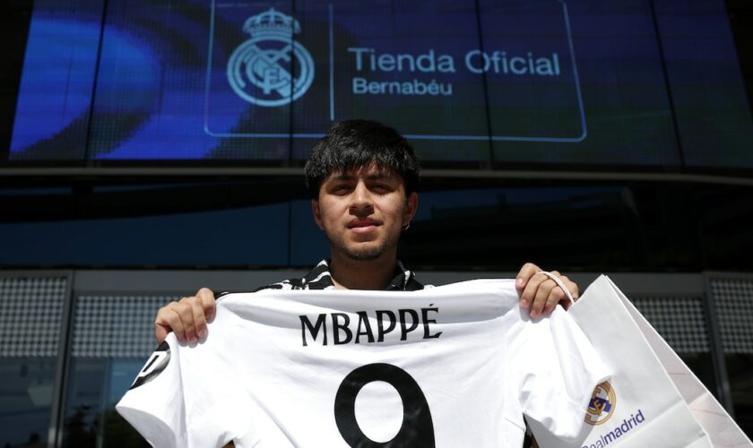 Un supporteur pose avec un maillot du Real floqué Kylian Mbappé, devant une boutique du club, le 11 juillet 2024 à Madrid