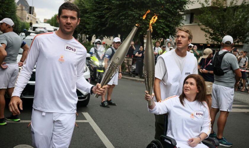 Press agency photographer Christina Assi, right, holds the Olympic torch with. Nicolas Payeur, left, at the 2024 Summer Olympics, Sunday, July 21, 2024, in Vincennes, outside Paris, France. Assi was struck by a tank shell on Oct. 13, 2023 while reporting clashes between the Israeli army and armed groups in southern Lebanon. (AP Photo/Thomas Padilla)