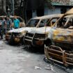 Security personnel walk past damaged vehicles of a government owned organization in Dhaka