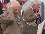 King Charles battles a gust of wind as he exits Sunday service at Caithness church in Scotland - as the monarch is forced to take grab his head to steady himself