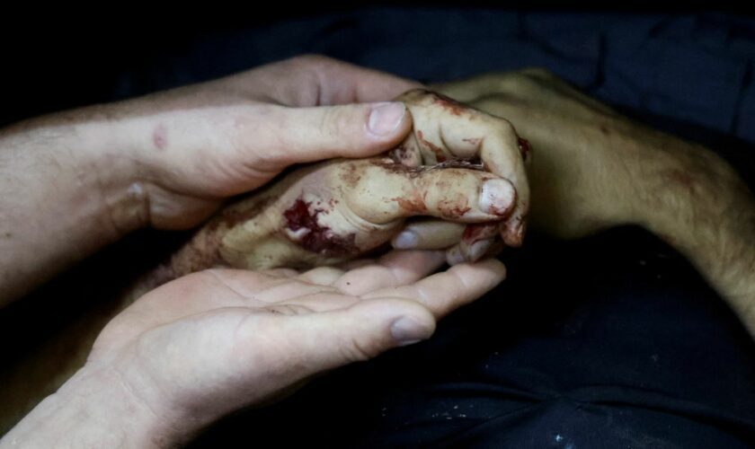 A person holds the hand of a Palestinian killed in an Israeli air strike on a car, at a morgue in Tubas. Pic: Reuters