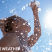 A woman pours water on herself from a plastic bottle as the sun beats down from a clear blue sky.