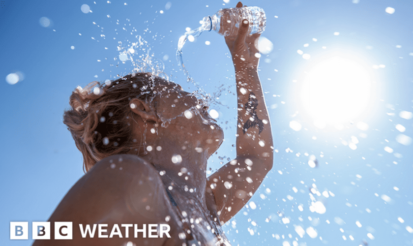 A woman pours water on herself from a plastic bottle as the sun beats down from a clear blue sky.