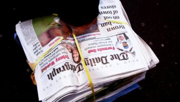 A newsagent carries a pile of Daily Telegraph newspapers