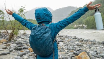 Wasserdichter Rucksack: Frau steht in Regenjacke und mit Rucksack an einem Fluss