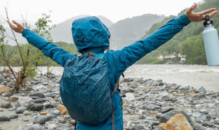 Wasserdichter Rucksack: Frau steht in Regenjacke und mit Rucksack an einem Fluss