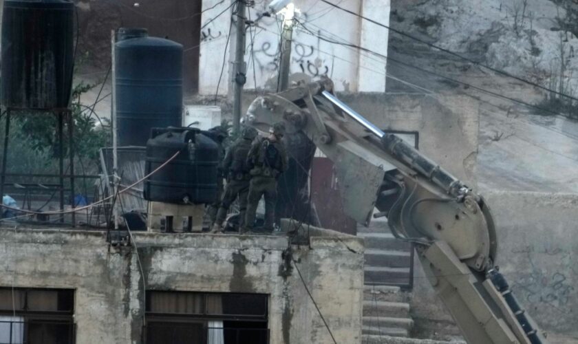 Israeli soldiers look over a rooftop where two bodies lie motionless in the West Bank town of Qabatiya. Pic: AP