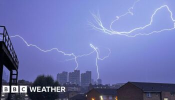 Fork lightning fills the darkened sky with some lightning hitting high rise buildings in the distance