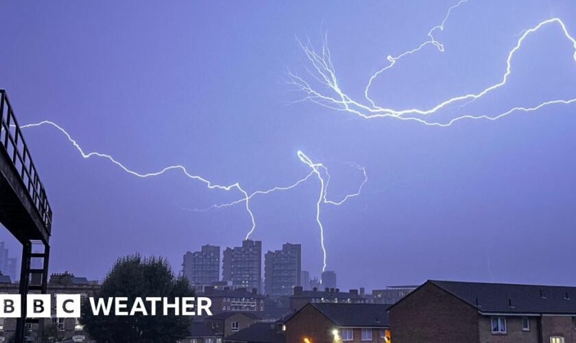 Fork lightning fills the darkened sky with some lightning hitting high rise buildings in the distance