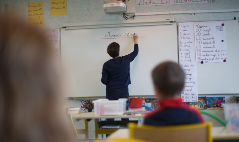 A teacher wearing a protective face mask works with pupils after they have returned to their classroom at the Trinite public school in the Groix island, on May 12, 2020, two days after France eased lockdown measures to curb the spread of the COVID-19 pandemic, caused by the novel coronavirus. (Photo by Loic VENANCE / AFP)