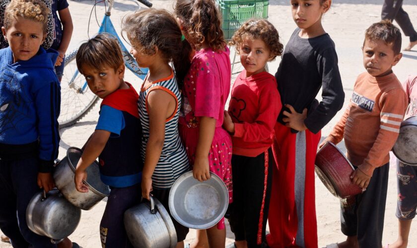 Palestinian children queue to receive food cooked by a charity kitchen  in Khan Younis