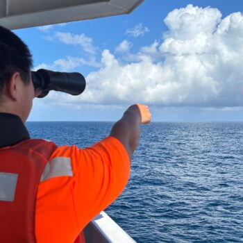 Photo diffusée par les gardes-côtes taïwanais, le 14 octobre 2024, d'un garde-côte taïwanais, sur un navire pétrolier au large de l'îlot Pengjia, observant aux jumelles un navire des gardes-côtes chinois naviguant en dehors des eaux territoriales de Taïwan