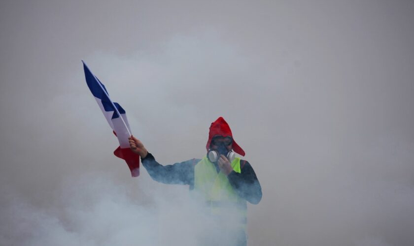 Un "gilet jaune" tient le drapeau français dans la fumée des gaz lacrymogènes lors d'une manifestation contre la hausse du coût de la vie, le 1er décembre 2018 à Paris