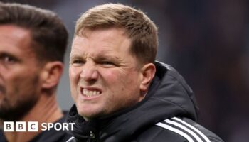 Eddie Howe and one other person talk as they kneel on a pitch