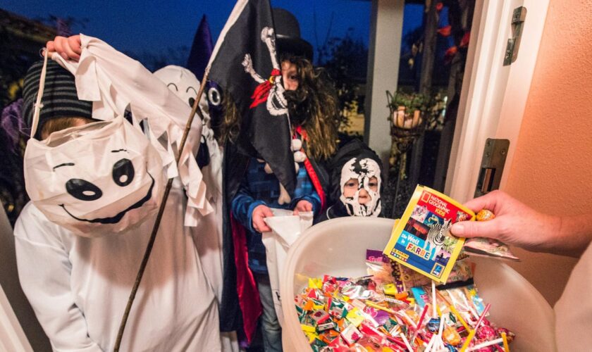 Kinder bekommen zu Halloween Süßigkeiten an einer Haustür