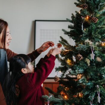 Mutter und Kind schmücken einen Tannenbaum.