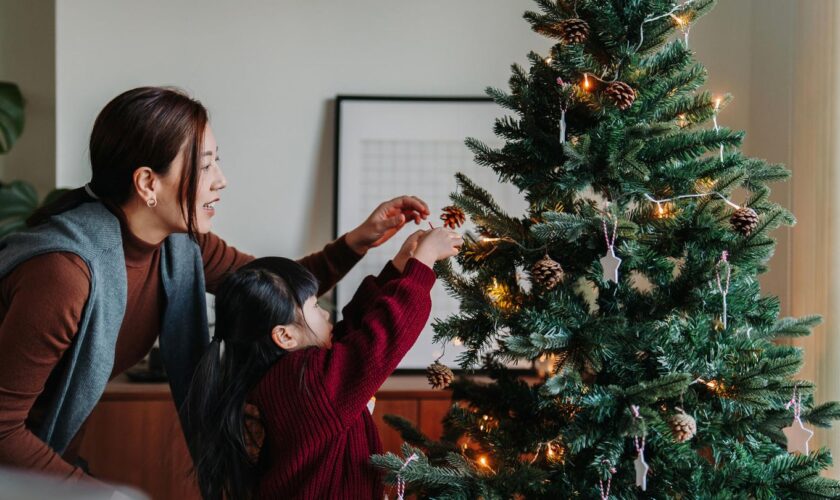 Mutter und Kind schmücken einen Tannenbaum.