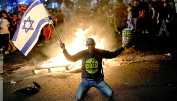 A protester holds an Israeli flag as Israelis light a bonfire during a protest after Prime Minister Benjamin Netanyahu has dismissed his defense minister Yoav Gallant in a surprise announcement in Tel Aviv, Israel, Tuesday, Nov. 5, 2024. (AP Photo/Francisco Seco)