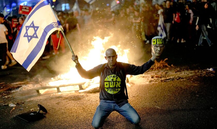 A protester holds an Israeli flag as Israelis light a bonfire during a protest after Prime Minister Benjamin Netanyahu has dismissed his defense minister Yoav Gallant in a surprise announcement in Tel Aviv, Israel, Tuesday, Nov. 5, 2024. (AP Photo/Francisco Seco)