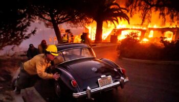 Firefighters and sheriff's deputies push a vintage car away from a burning home as the Mountain Fire burns in Camarillo, Calif., on Wednesday, Nov. 6, 2024. (AP Photo/Noah Berger)