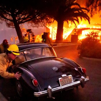 Firefighters and sheriff's deputies push a vintage car away from a burning home as the Mountain Fire burns in Camarillo, Calif., on Wednesday, Nov. 6, 2024. (AP Photo/Noah Berger)