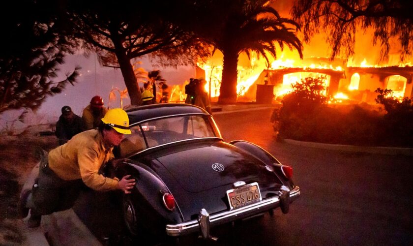 Firefighters and sheriff's deputies push a vintage car away from a burning home as the Mountain Fire burns in Camarillo, Calif., on Wednesday, Nov. 6, 2024. (AP Photo/Noah Berger)