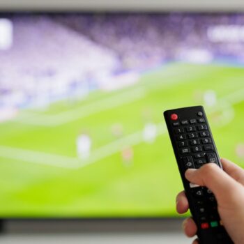 Close up of hand with remote controller and tv with football on background