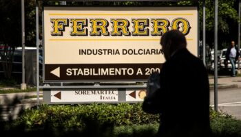 Cette photo prix le 29 mai 2019 à Alba montre un homme marchant près du logo du fabricant italien de chocolat de marque Ferrero.