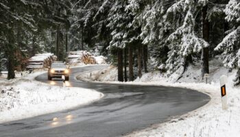 Ein Auto fährt auf einer nassen Straße durch einen Wald voller Schnee