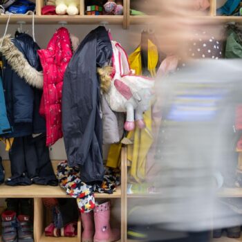 Ein Kind einer Kindergartengruppe läuft an der vollen Garderobe vorbei