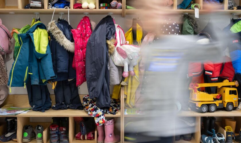 Ein Kind einer Kindergartengruppe läuft an der vollen Garderobe vorbei