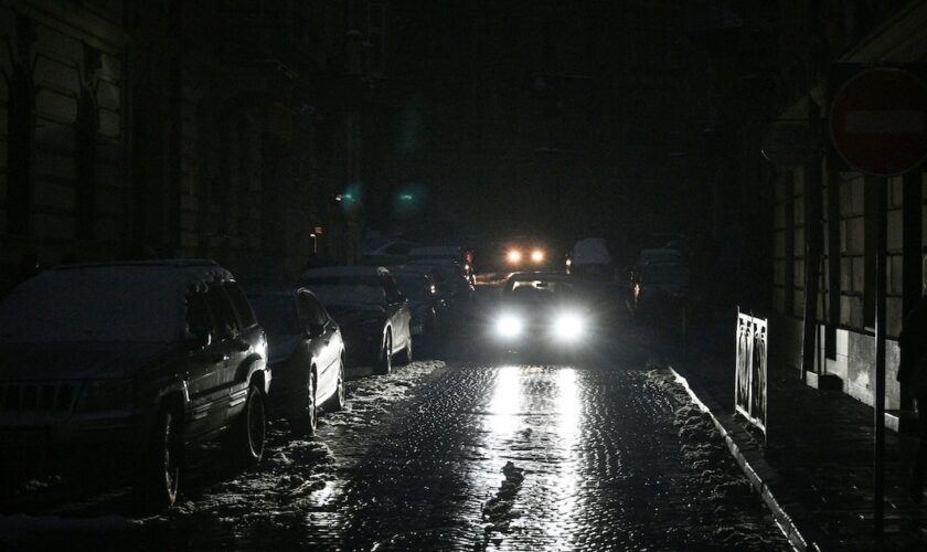 Des voitures empruntent une rue de Lviv (Ukraine) plongée dans le noir en raison de coupures d'électricité le 24 novembre 2022