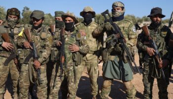 Syrian opposition fighters stand in formation after entering the village of Anjara, western outskirts of Aleppo, Syria, Thursday Nov. 28, 2024, part of  their major offensive on government-controlled areas in the country's northwestern Syria. (AP Photo/Omar Albam)