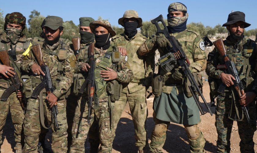 Syrian opposition fighters stand in formation after entering the village of Anjara, western outskirts of Aleppo, Syria, Thursday Nov. 28, 2024, part of  their major offensive on government-controlled areas in the country's northwestern Syria. (AP Photo/Omar Albam)