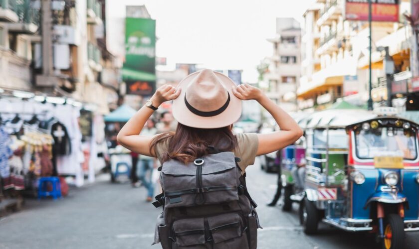 Eine Frau mit Sonnenhut läuft durch eine belebte Straße in Bangkok.