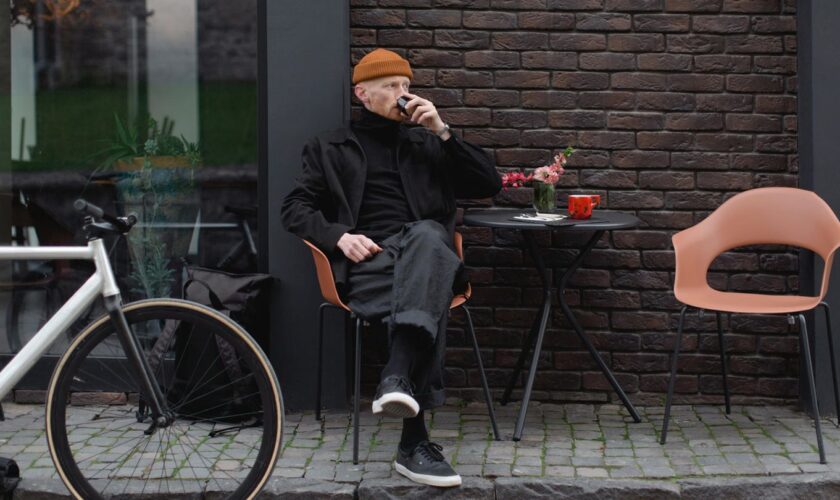 Ein Mann im Winter, der vor einem Caffe sitzt und seinen Kaffe trinkt