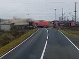 Death-defying moment truck driver stuck at railway level crossing leaps from vehicle just as a freight train smashes into it