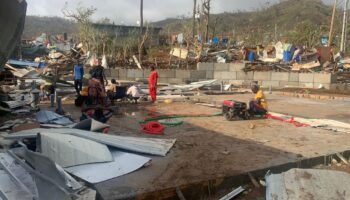 Des habitants assis au milieu de tas de débris de tôles et de bois après la destruction de leurs maisons par le cyclone Chido qui a frappé Mayotte, le 15 décembre 2024