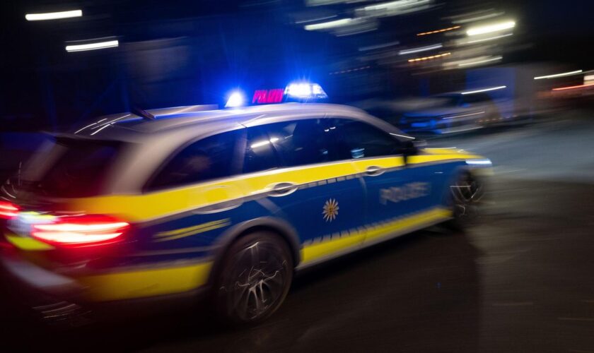 Ein Polizeifahrzeug fährt mit Blaulicht an einem Gebäude vorbei