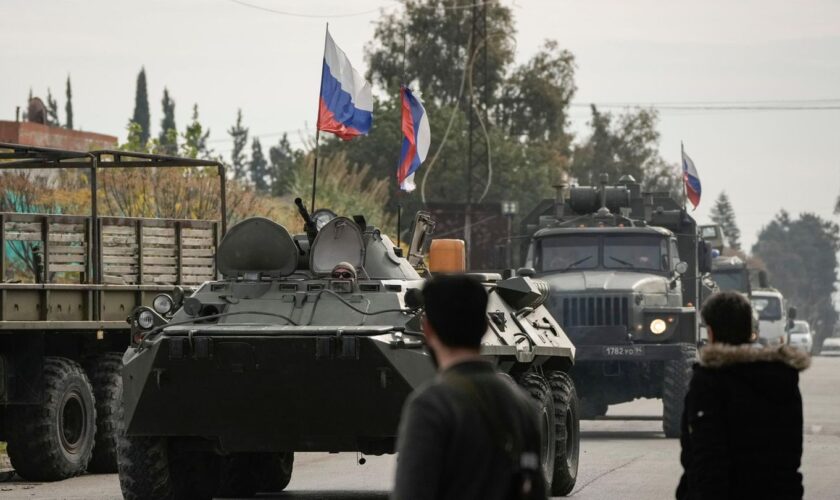 Kämpfer aus Syrien beobachten die Vorbeifahrt russischer Panzerfahrzeuge in der Nähe des syrischen Luftwaffenstützpunkts Hmeimim