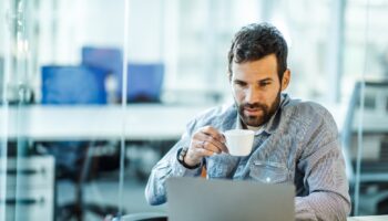 Male entrepreneur reading an e-mail on his computer while drinking coffee.