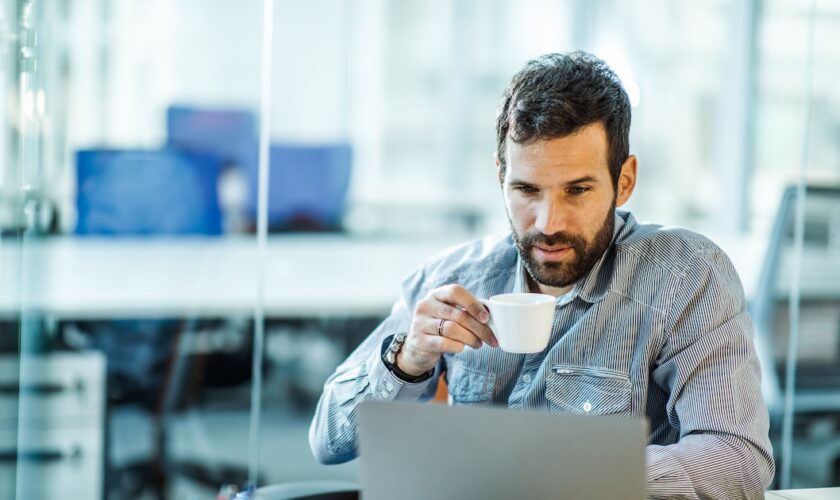 Male entrepreneur reading an e-mail on his computer while drinking coffee.