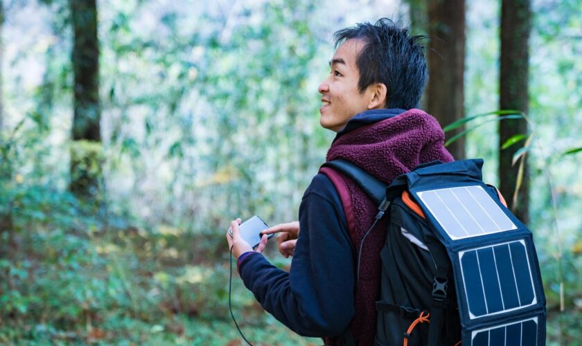 Mann mit Solarzellen, um Smartphone im Wald zu versorgen