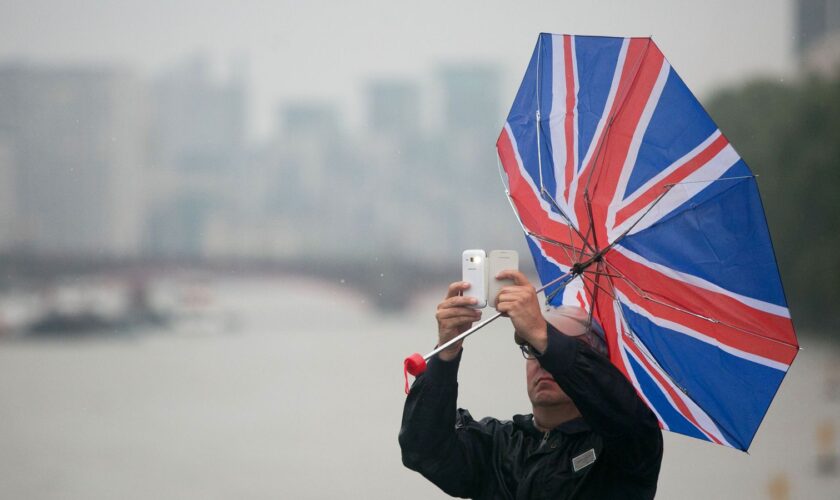 File photo dated 13/08/15 of a man's umbrella blowing inside out as he take a photo with his mobile phone in Westminster, London. Pic: PA