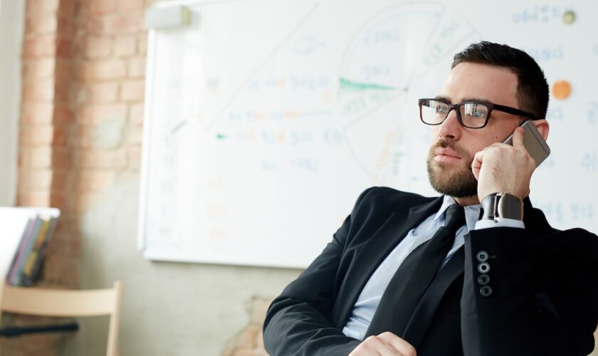 Confident employer calling by mobile phone in office